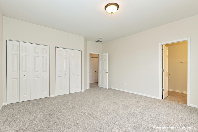 unfurnished bedroom featuring baseboards, carpet flooring, visible vents, and two closets