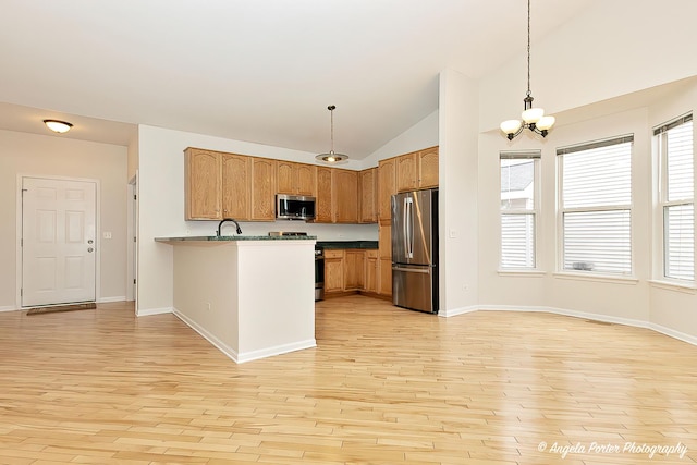 kitchen featuring light wood-type flooring, a chandelier, a sink, a peninsula, and appliances with stainless steel finishes