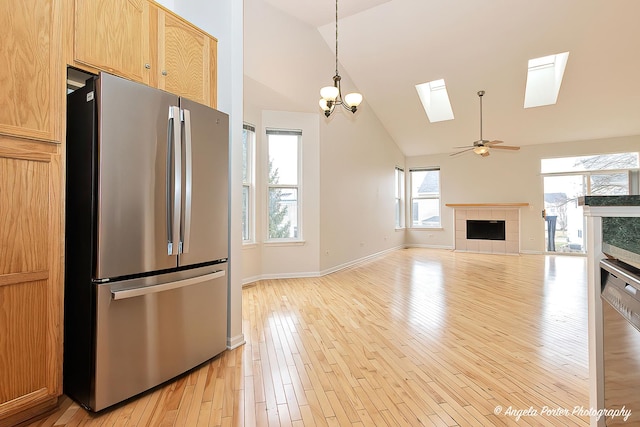 kitchen with stainless steel appliances, high vaulted ceiling, a skylight, light wood-style flooring, and a fireplace