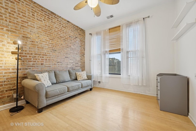 living area featuring light wood finished floors, visible vents, ceiling fan, brick wall, and baseboards