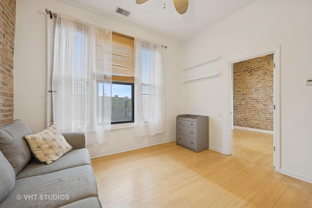 living room with baseboards, visible vents, brick wall, ceiling fan, and wood finished floors