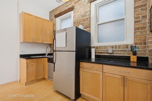 kitchen with stainless steel appliances, a sink, brick wall, light wood-type flooring, and dark stone counters