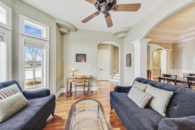 living area with ornate columns, arched walkways, baseboards, light wood-style flooring, and a ceiling fan