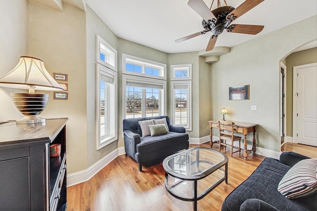 living area with arched walkways, a ceiling fan, baseboards, and light wood finished floors