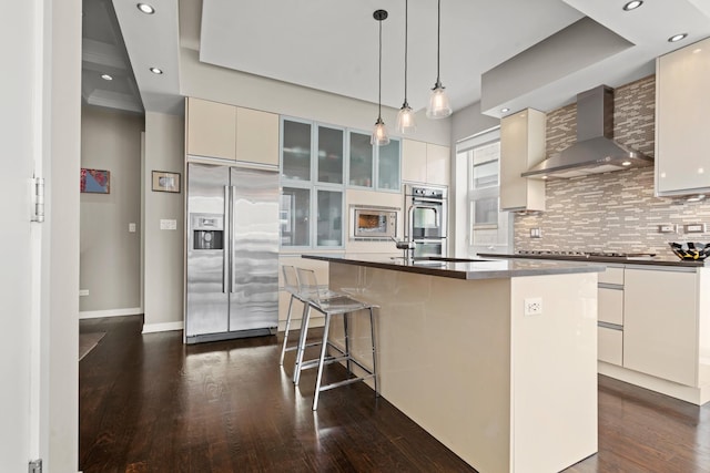 kitchen featuring wall chimney range hood, stainless steel appliances, white cabinets, and a center island with sink