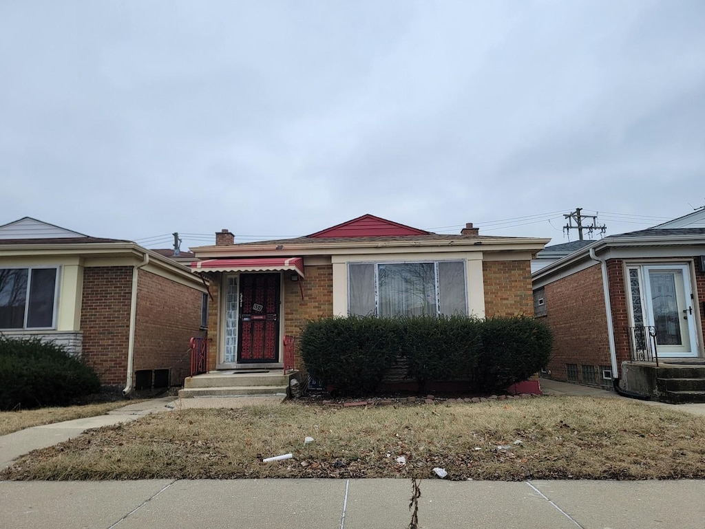 bungalow with a chimney and brick siding