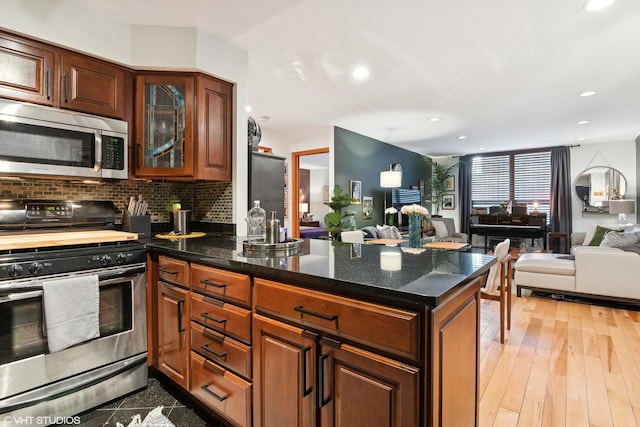 kitchen featuring tasteful backsplash, stainless steel appliances, dark stone countertops, and light wood-type flooring