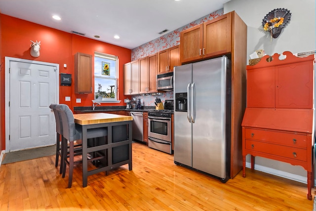 kitchen featuring stainless steel appliances, butcher block countertops, visible vents, light wood-type flooring, and brown cabinets