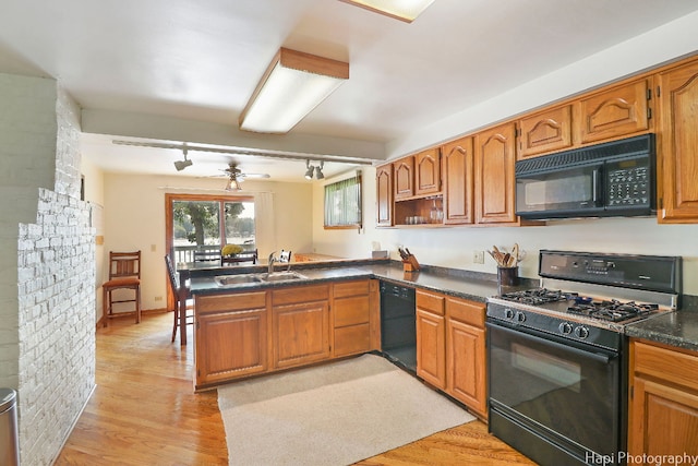 kitchen with sink, rail lighting, black appliances, kitchen peninsula, and light wood-type flooring