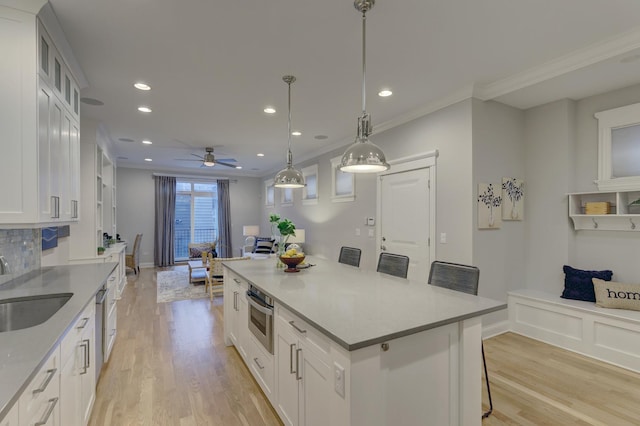 kitchen featuring a breakfast bar, sink, pendant lighting, stainless steel oven, and white cabinets