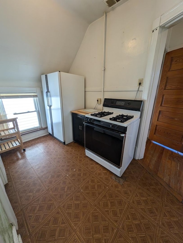 kitchen with range with gas stovetop, vaulted ceiling, and white fridge