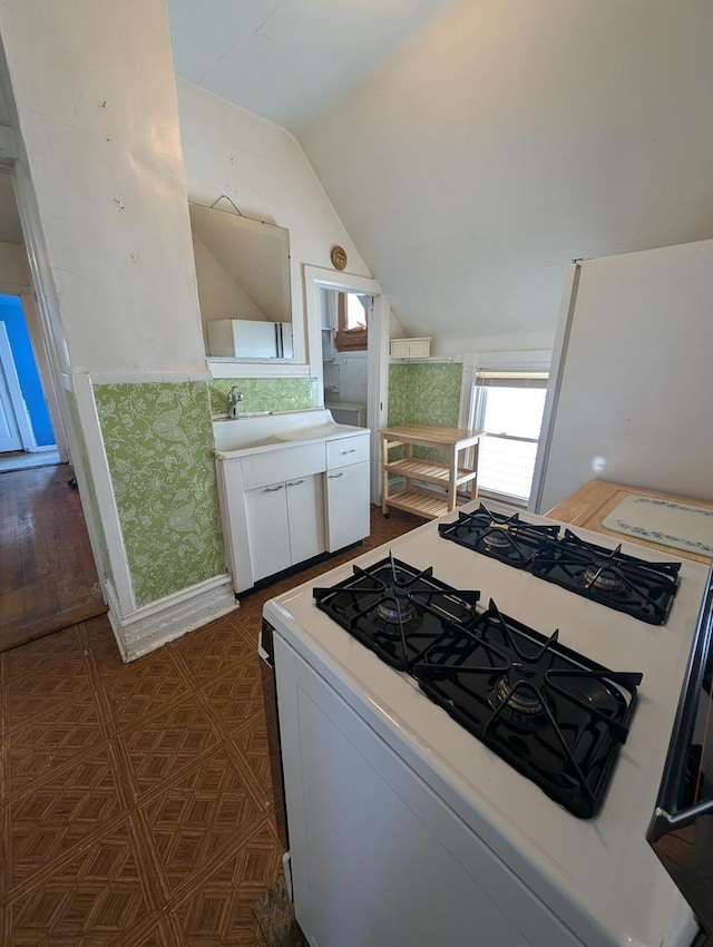 kitchen with lofted ceiling, sink, range with gas stovetop, and white cabinets