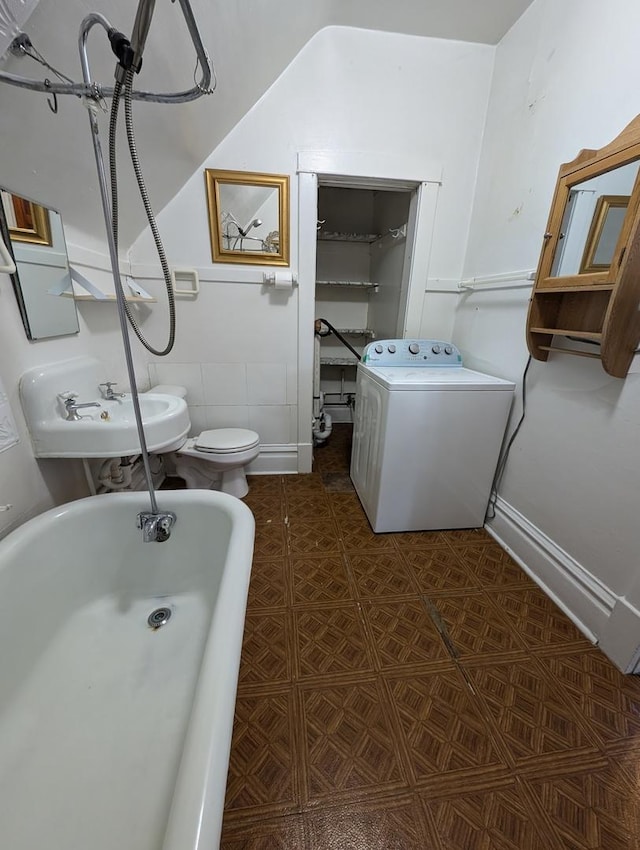 bathroom with washer / clothes dryer, a bathing tub, sink, and toilet