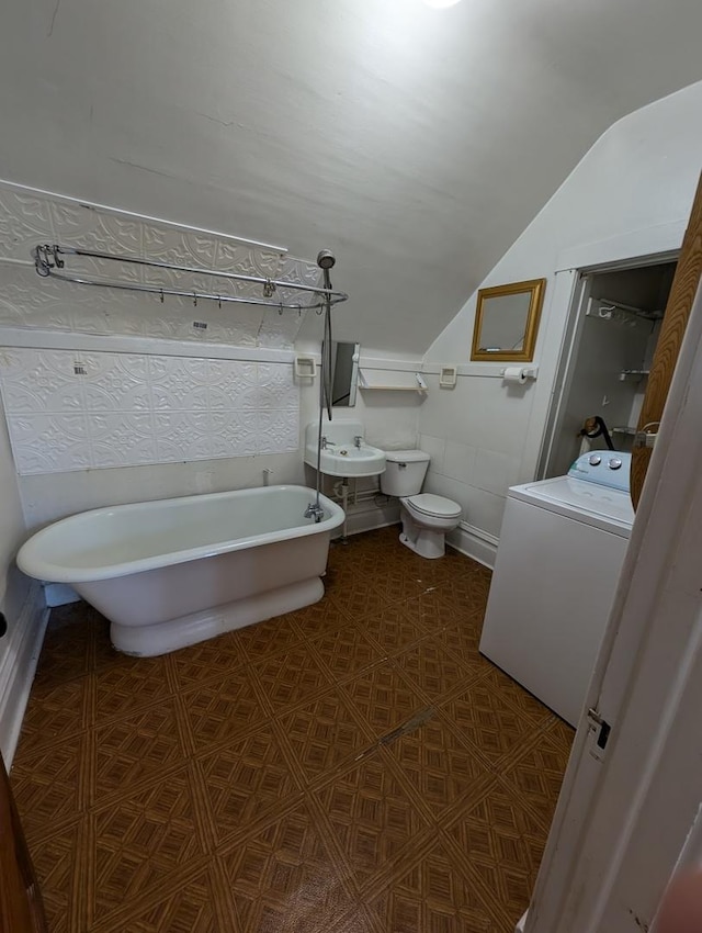 bathroom featuring lofted ceiling, toilet, sink, a bath, and washer / clothes dryer