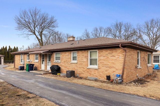 exterior space featuring a shingled roof, a chimney, central AC, and brick siding