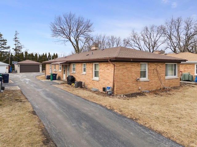 view of front of property with a garage, a chimney, an outdoor structure, central AC, and brick siding