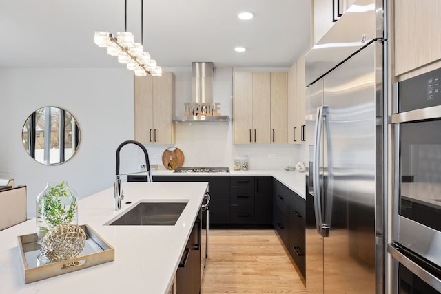 kitchen featuring modern cabinets, appliances with stainless steel finishes, light countertops, wall chimney range hood, and a sink