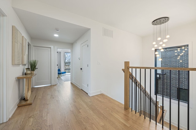 hall featuring a chandelier, wood finished floors, visible vents, baseboards, and an upstairs landing