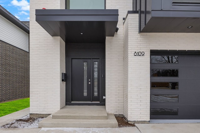 doorway to property featuring a garage and brick siding