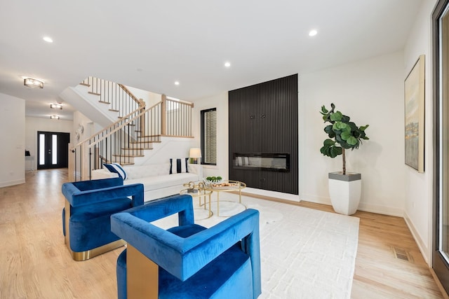 living room with light wood-type flooring, a large fireplace, stairs, and recessed lighting