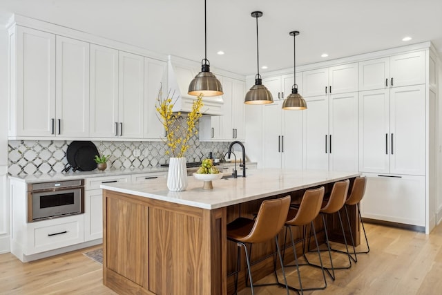 kitchen featuring an island with sink, white cabinetry, hanging light fixtures, and stainless steel oven