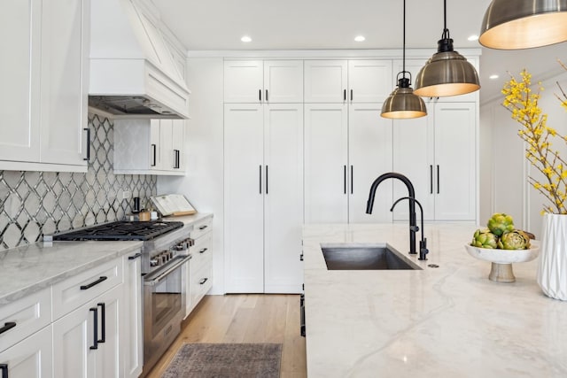 kitchen featuring high end range, light stone countertops, custom exhaust hood, white cabinetry, and a sink