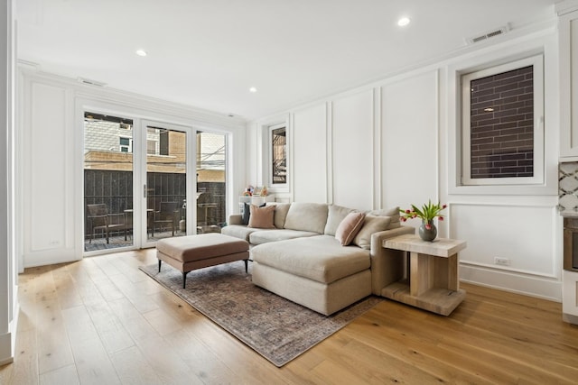 living room featuring recessed lighting, a decorative wall, visible vents, ornamental molding, and light wood-type flooring