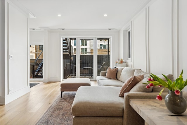 living area with light wood-type flooring, crown molding, stairs, and a wealth of natural light