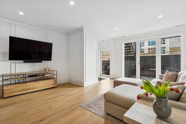 living room featuring crown molding, light wood-type flooring, a decorative wall, and recessed lighting