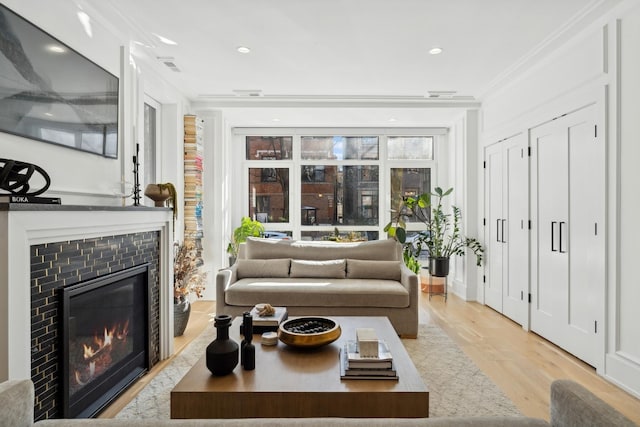 living room with ornamental molding, recessed lighting, a tile fireplace, and light wood-style floors