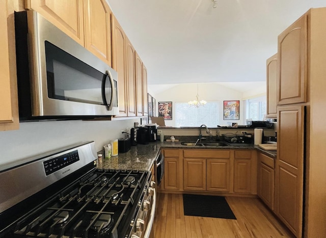 kitchen featuring sink, vaulted ceiling, appliances with stainless steel finishes, dark stone counters, and light hardwood / wood-style floors