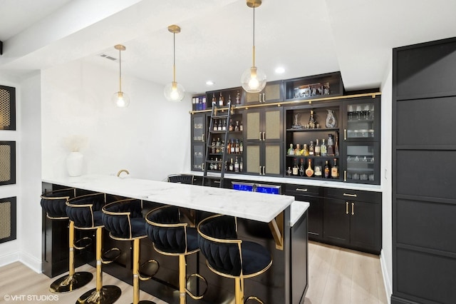 bar with hanging light fixtures, light wood-type flooring, indoor wet bar, and visible vents