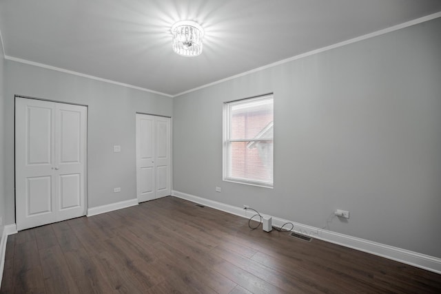 unfurnished bedroom with ornamental molding, two closets, and dark hardwood / wood-style flooring