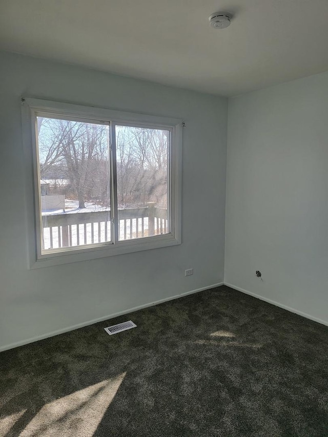 empty room featuring visible vents, plenty of natural light, baseboards, and dark carpet