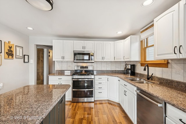 kitchen featuring dark stone counters, a sink, stainless steel appliances, light wood-style floors, and backsplash