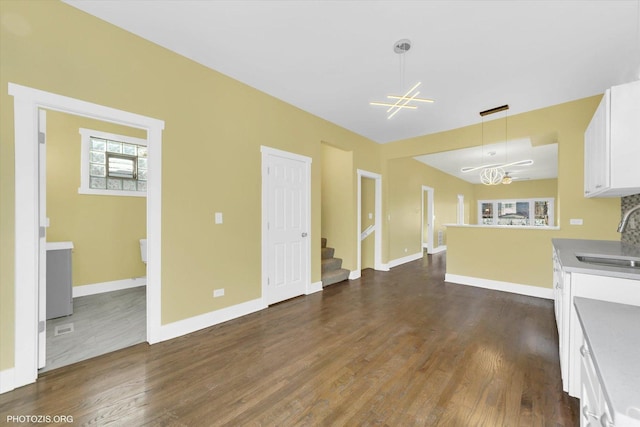 unfurnished living room with a chandelier, dark wood-type flooring, a sink, and baseboards