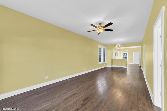 unfurnished living room featuring baseboards, visible vents, dark wood-type flooring, and ceiling fan with notable chandelier