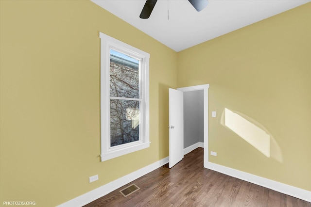 empty room featuring dark wood-style floors, a ceiling fan, visible vents, and baseboards