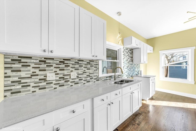 kitchen featuring dark wood-style flooring, backsplash, white cabinets, a sink, and light stone countertops