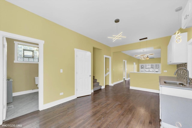 unfurnished living room featuring a notable chandelier, a sink, baseboards, stairs, and dark wood-style floors