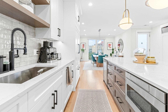 kitchen featuring pendant lighting, sink, light stone counters, and white cabinets