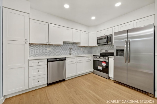 kitchen with appliances with stainless steel finishes, white cabinetry, sink, backsplash, and light hardwood / wood-style floors