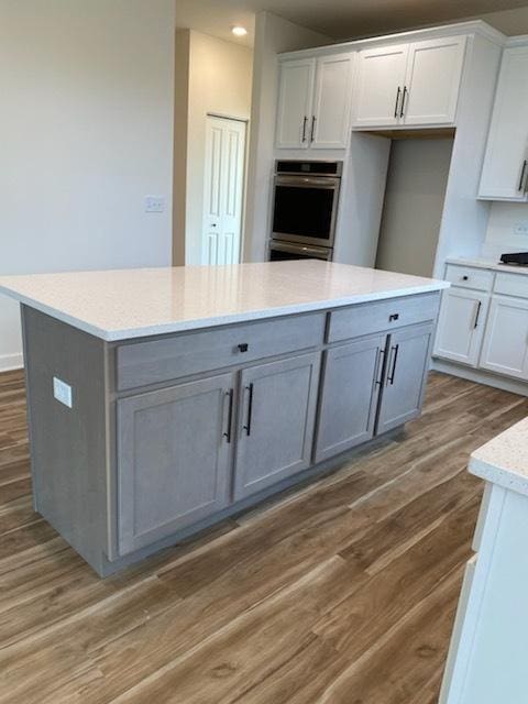 kitchen featuring a center island, wood finished floors, stainless steel double oven, white cabinetry, and recessed lighting