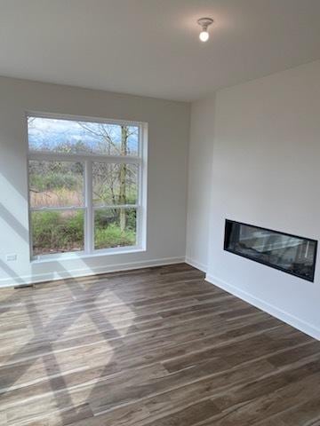 unfurnished living room featuring baseboards, a glass covered fireplace, and wood finished floors