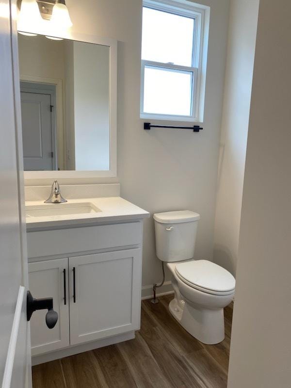 bathroom with toilet, vanity, wood finished floors, and baseboards