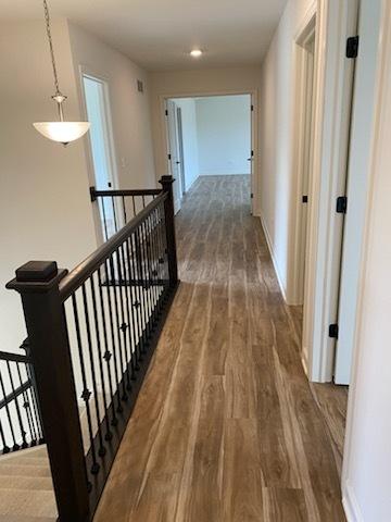 hall featuring baseboards, wood finished floors, an upstairs landing, and recessed lighting