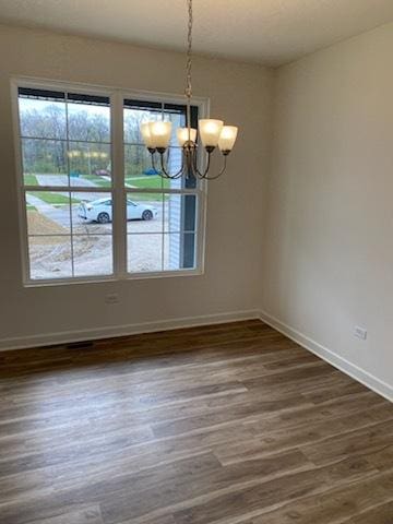 unfurnished dining area with dark wood finished floors, baseboards, and an inviting chandelier