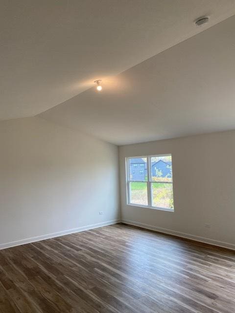 empty room with dark wood-type flooring, vaulted ceiling, and baseboards