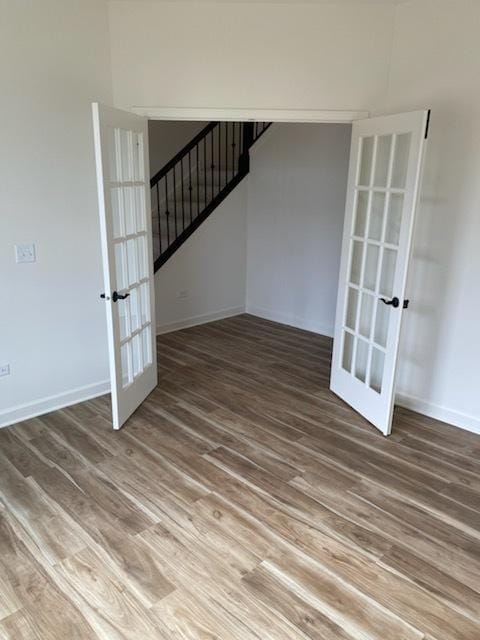 unfurnished living room with wood finished floors, stairs, baseboards, and french doors