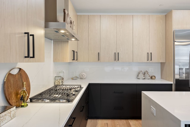 kitchen featuring wall chimney exhaust hood, light brown cabinets, stainless steel appliances, and modern cabinets